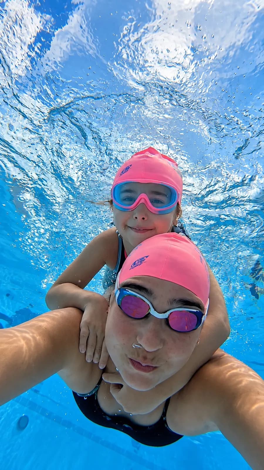 Mãe e filha de touca rosa e óculos mergulhando juntas, foto subaquática