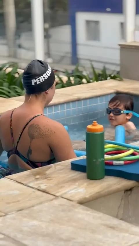 Professora com touca “Personal” orientando uma criança na borda da piscina